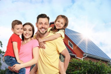 Evlerinin yakınında güneş panelleri olan mutlu bir aile. Alternatif enerji kaynağı