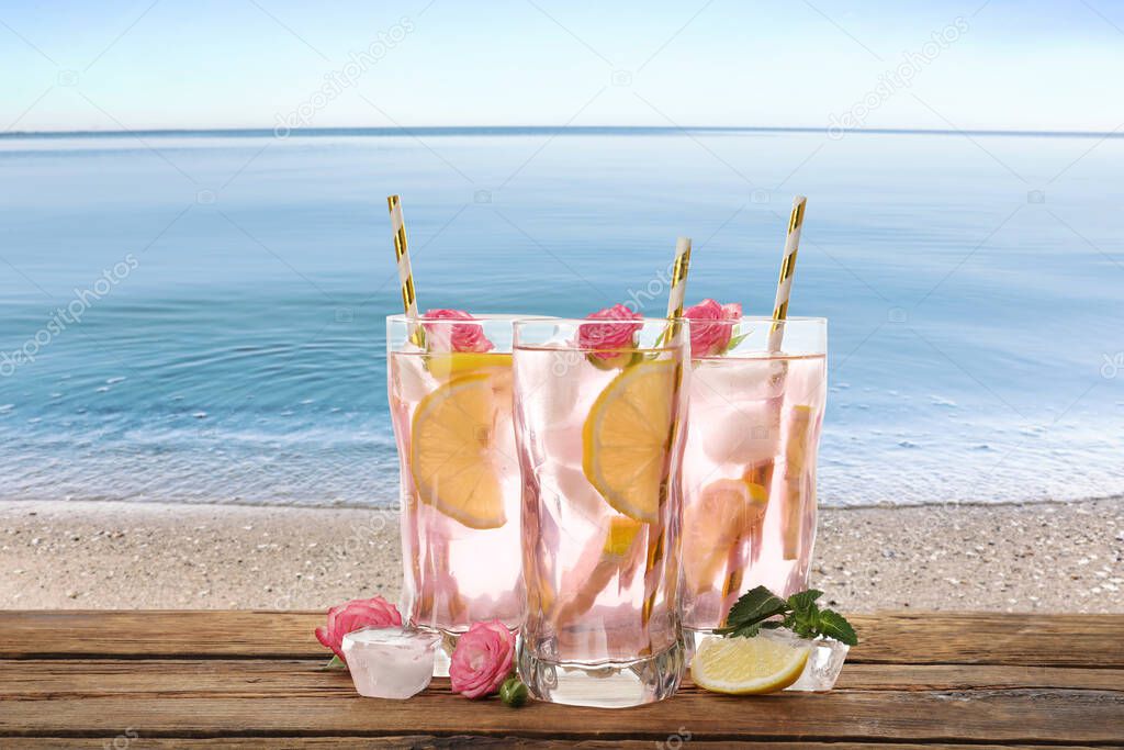 Tasty refreshing drink on wooden table against sandy beach