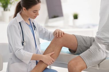 Kadın ortopedist klinikte hastanın bacağını muayene ediyor.