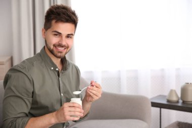 Oturma odasında lezzetli yoğurtlu mutlu genç adam. Metin için boşluk