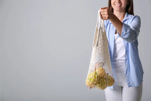 Woman holding net bag with fresh ripe pears on grey background, closeup. Space for text
