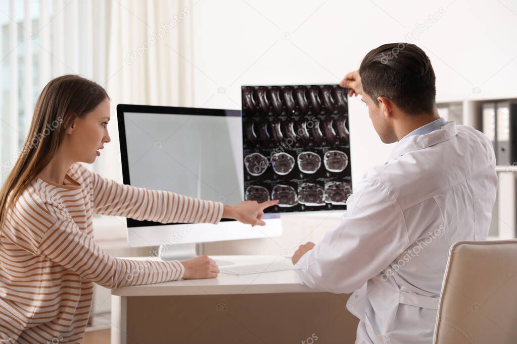 Orthopedist showing X-ray picture to patient at table in clinic