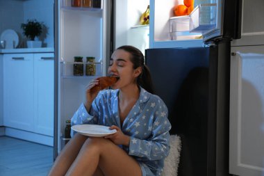 Geceleri açık buzdolabının yanında çörek yiyen genç bir kadın.