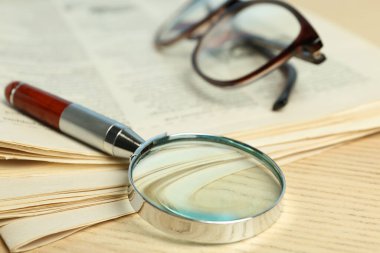 Bir yığın gazete, büyüteç ve tahta masanın üzerinde gözlük. Arama konsepti
