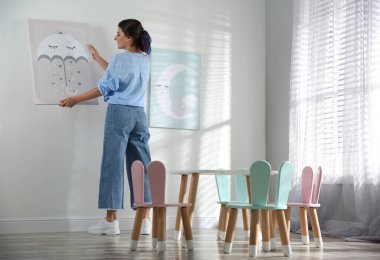 Dekoratör beyaz duvara resim asıyor. Çocuk odası iç tasarımı.