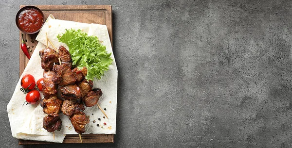 Wooden board with delicious barbecued meat and space for text on gray table, top view. Banner design