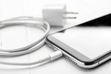 Akıllı telefon ve USB şarj aleti beyaz ahşap masada, yakın plan. Modern teknoloji