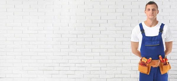 Electrician with tools near white brick wall, space for text. Banner design