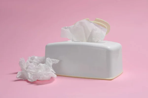 Holder with paper tissues and used crumpled napkins on pink background