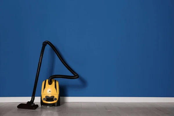 Modern yellow vacuum cleaner on floor near blue wall, space for text