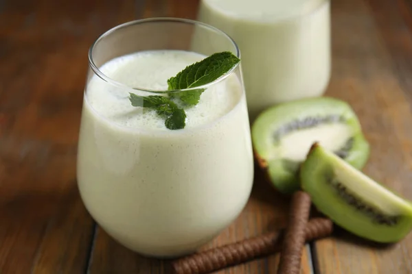 Tasty milk shake with kiwi on wooden table, closeup