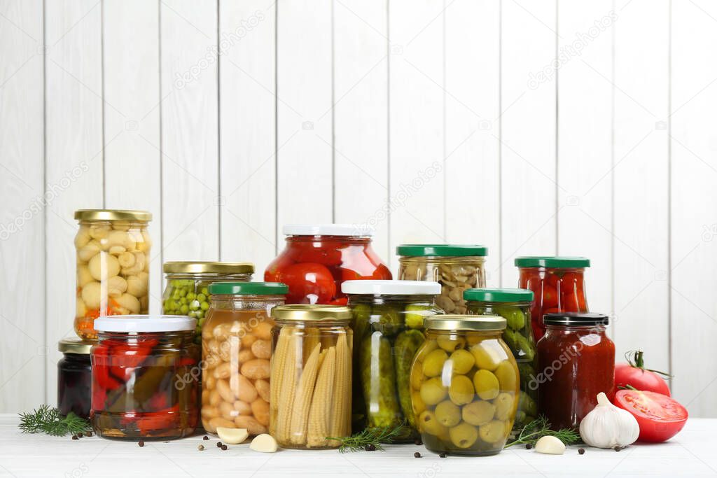 Glass jars with different pickled vegetables and mushrooms on white wooden background