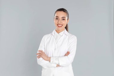 Açık gri arka planda laboratuvar önlüklü mutlu genç kadın.