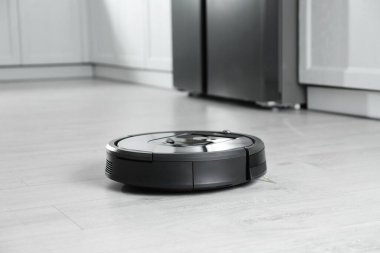 Mutfakta yerde modern robot süpürge var.