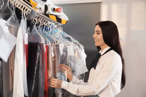 Female worker taking clothes from garment conveyor at dry-cleaner\'s