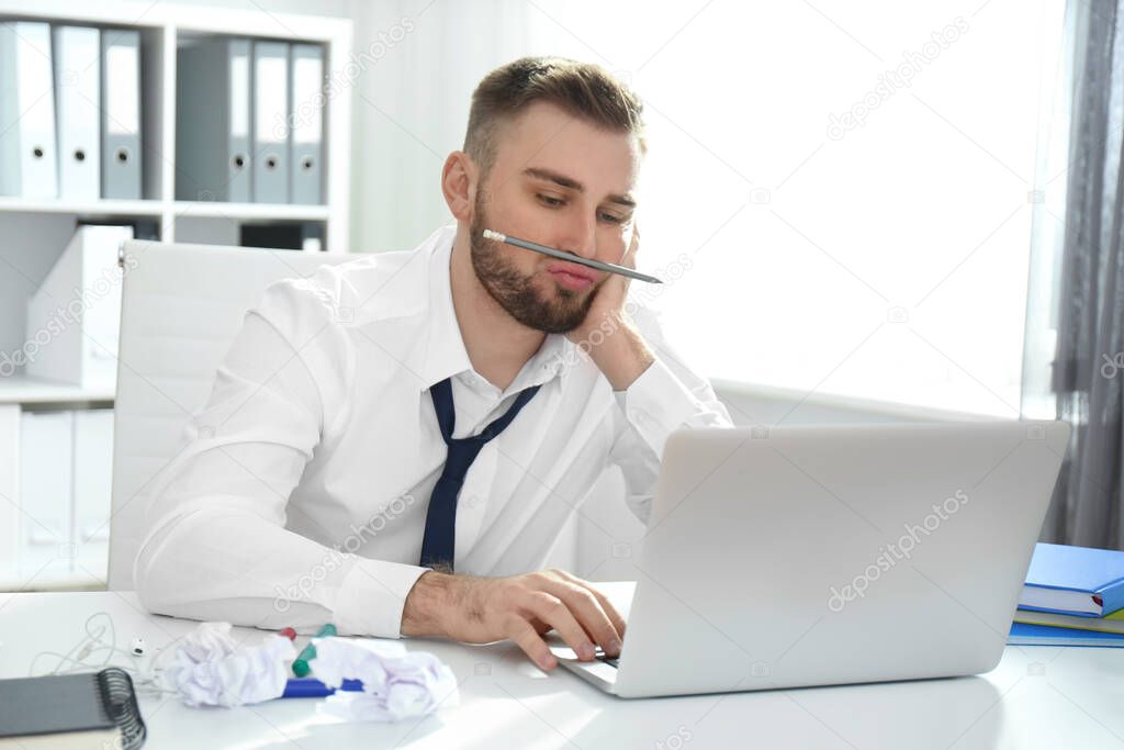 Lazy young man playing with pencil at messy table in office