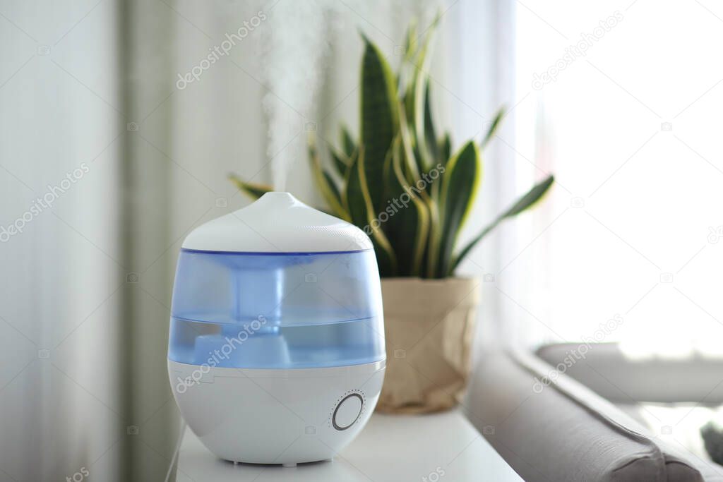 Modern air humidifier on table in living room. Space for text