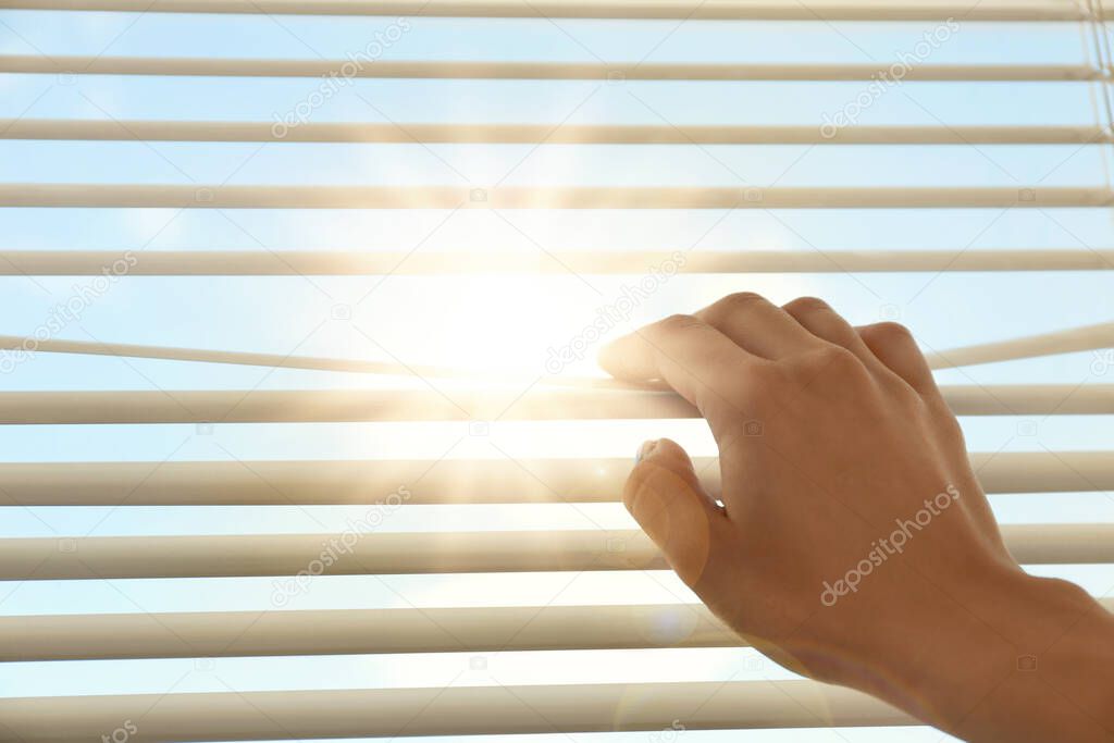 Woman opening window blinds on sunny morning, closeup