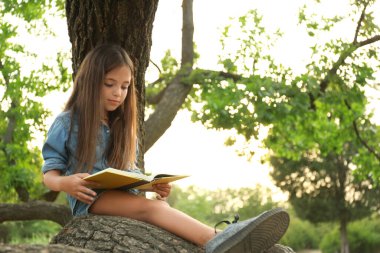 Parkta ağaçta kitap okuyan tatlı küçük kız.