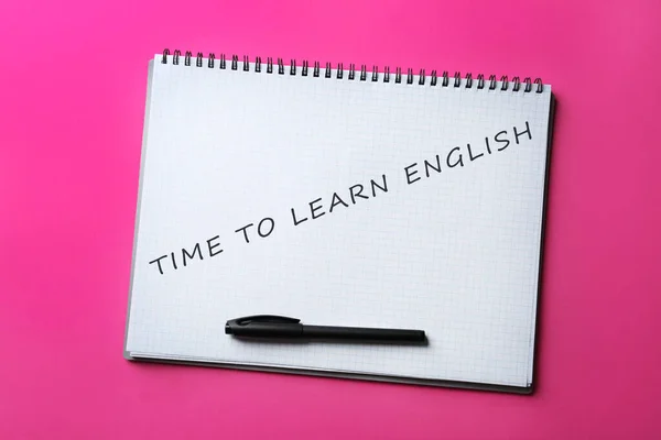 Open notebook with text Time To Learn English and pen on pink background, top view
