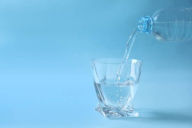 Açık mavi arka planda şişeden cama su dökmek. Metin için boşluk