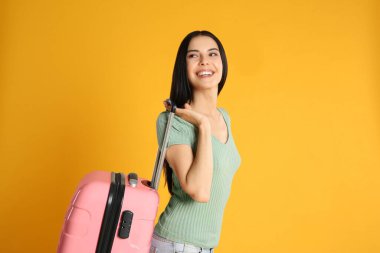 Sarı arka planda yaz gezisi için bavullu güzel bir kadın. Tatil gezisi