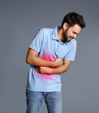 Gri arka planda mide ağrısı çeken bir adam.