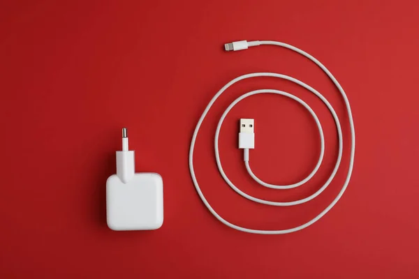 USB charge cable and adapter on red background, flat lay. Modern technology