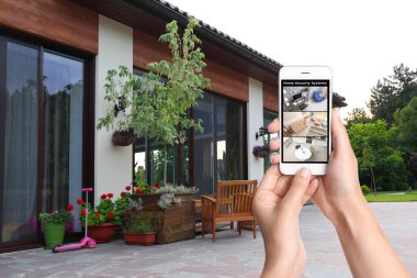 Alarm sistemi. Kadın arka bahçedeki akıllı telefondan modern CCTV kameralarını izliyor.