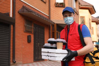 Koruyucu maskeli ve eldivenli bir kurye evin yakınlarında sipariş vermiş. Coronavirus karantinası sırasında yiyecek teslimatı