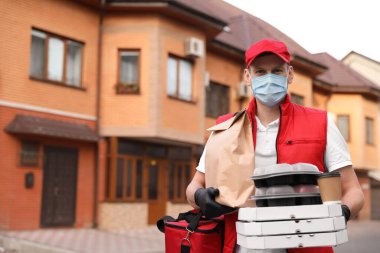 Koruyucu maskeli ve eldivenli bir kurye evin yakınlarında sipariş vermiş. Coronavirus karantinası sırasında yiyecek teslimatı