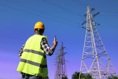 Yüksek voltaj kulesi yakınında taşınabilir radyo istasyonu olan profesyonel bir elektrikçi.