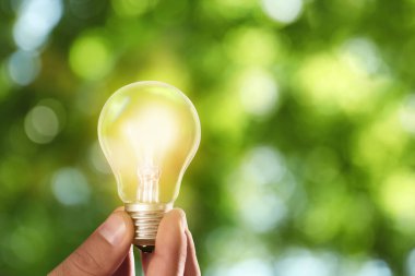Güneş enerjisi kavramı. Yeşil bulanık arka planda parlayan ampulü tutan adam, yakın plan
