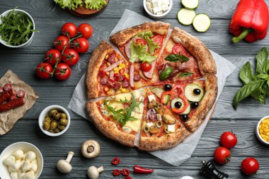 Düz kompozisyon, gri ahşap masada farklı lezzetli pizzaların dilimleriyle yatıyordu.