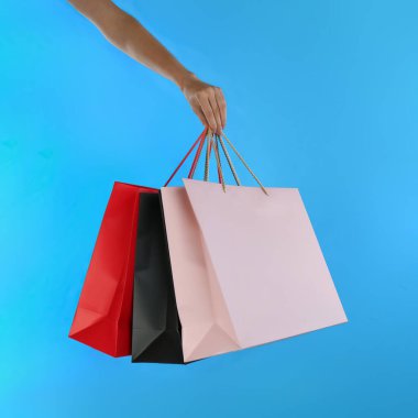 Açık mavi arka planda kağıt alışveriş torbaları olan kadın, yakın plan.