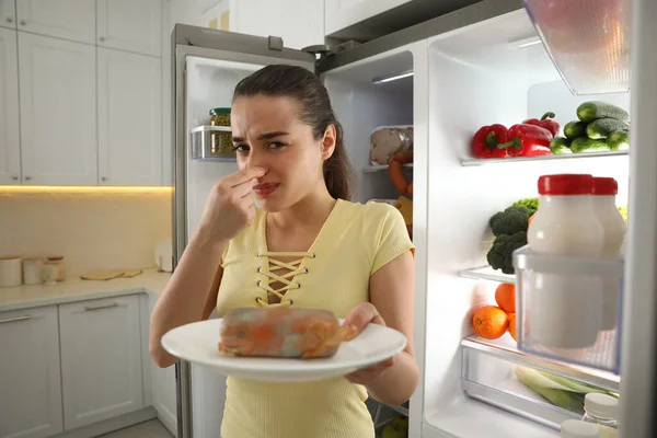 厨房里打开的冰箱旁边放着变质香肠的年轻女人 — 图库照片