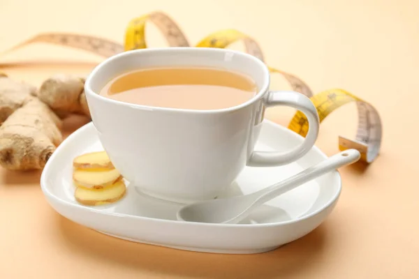 Cup of diet herbal tea and sliced ginger on orange background
