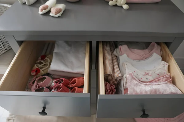 Open cabinet drawers with baby shoes and clothes in child room
