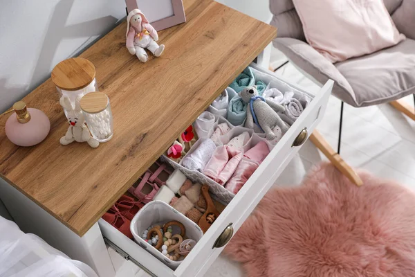 Modern open chest of drawers with baby clothes and accessories in room, above view