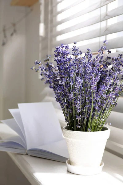 Beautiful lavender flowers and book on window sill indoors