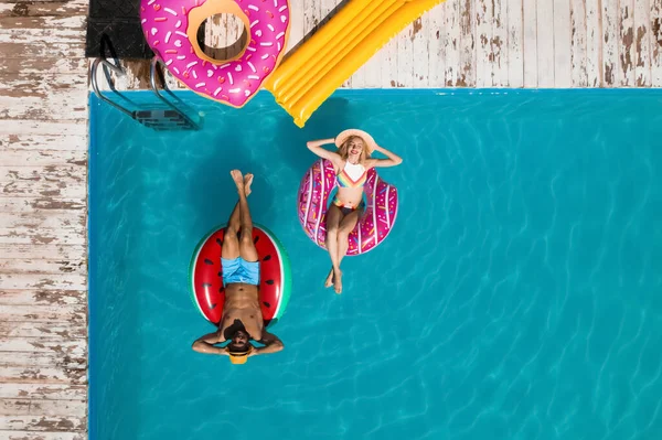 Happy couple with inflatable rings in swimming pool, top view. Summer vacation