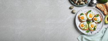 Açık gri mermer masa üzerinde bıldırcın yumurtası ve avokado ile lezzetli bruschetaların düz kompozisyonu, yazı için boşluk. Pankart tasarımı 