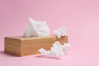 Kağıt mendilli tutucu ve pembe arka planda buruşmuş peçete kullanılmış.