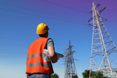 Yüksek voltaj kulesinin yanında evrakları olan profesyonel elektrikçi.