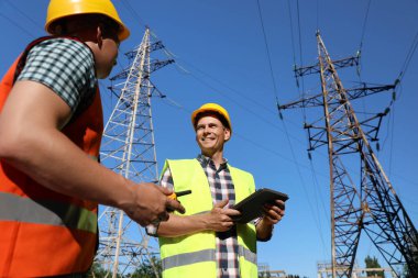 Yüksek voltaj kulelerinin yanında üniformalı profesyonel elektrikçiler.