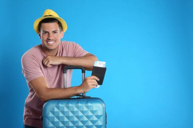 Çantalı ve pasaportlu bir adam mavi arka planda yaz gezisi için bilet almış. Tatil gezisi