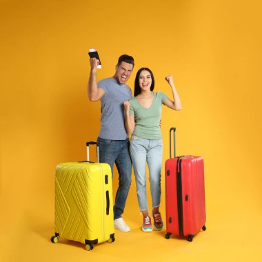 Sarı arka planda yaz gezisi için bavulları olan mutlu çift. Tatil gezisi