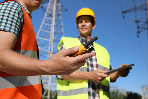 Professional electricians near high voltage towers, focus on hand with portable radio station