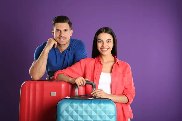 Happy couple with suitcases for summer trip on purple background. Vacation travel