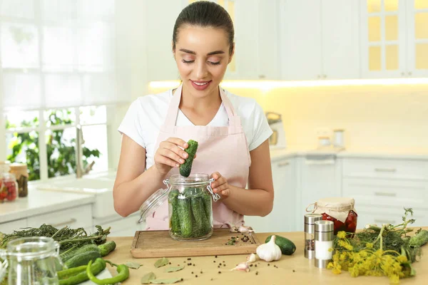 Mutfaktaki masada salatalık kavanozuna salatalık koyan kadın.